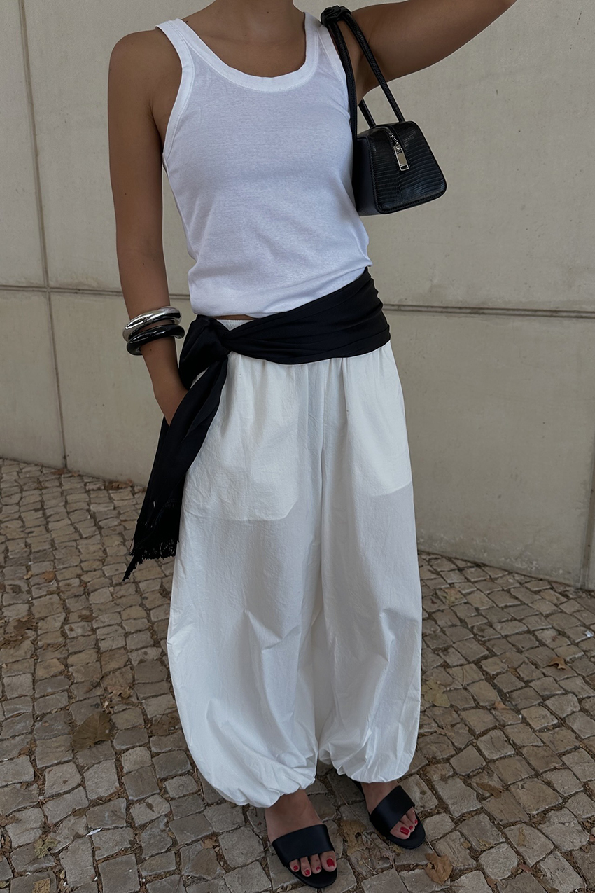 A woman wearing a white tank, white pants, and black scarf on her waist.