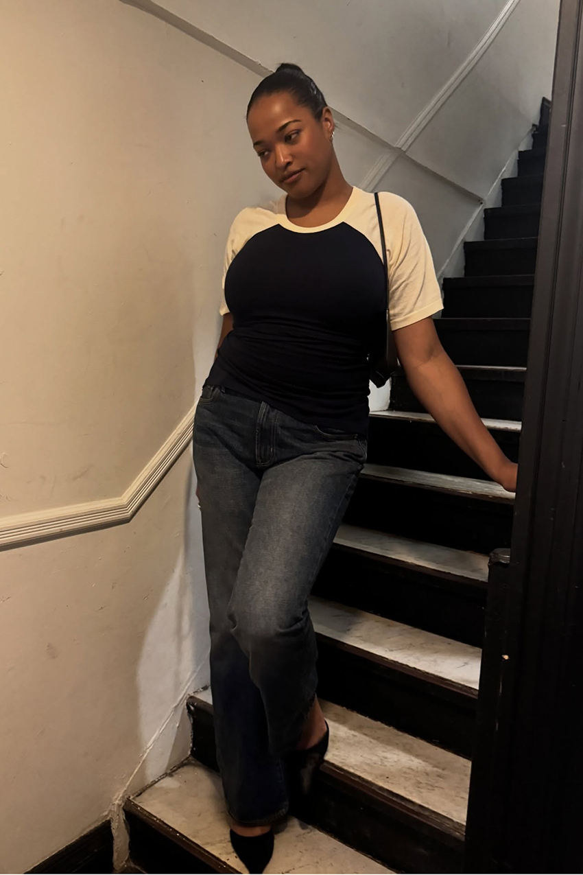 A woman wearing a white and black shirt, dark wash jeans, and pointed-toe shoes.
