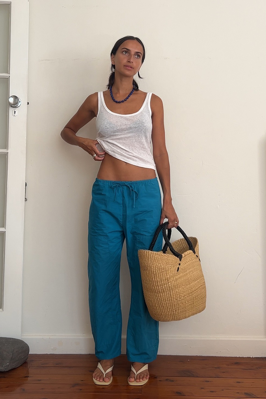 A woman wearing a white tank top, blue pants, and white sandals.